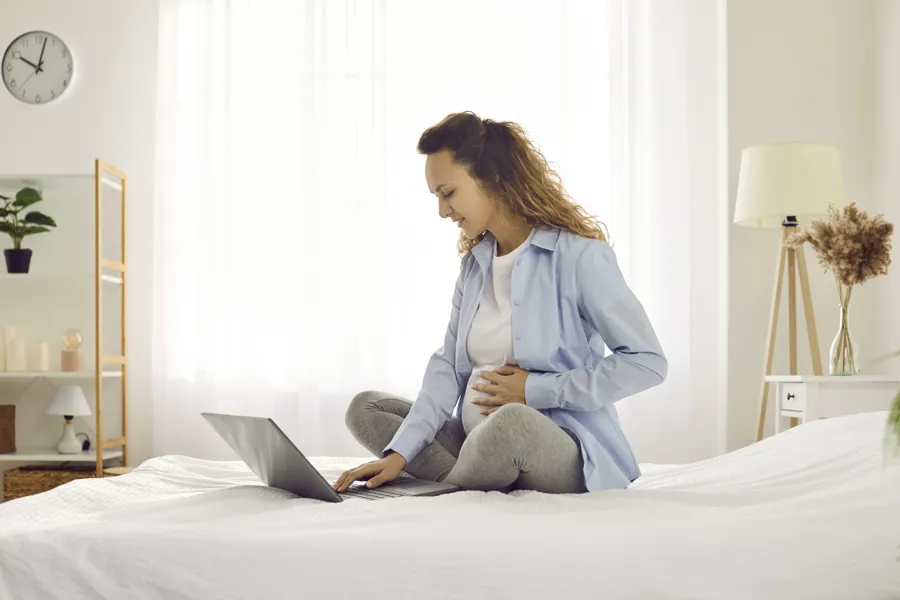 Gravid kvinne sitter på en seng