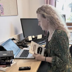 A researcher looking at a laptop with the handbook of nursing in her hands