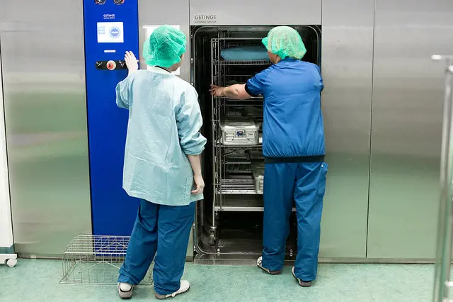 To ansatte som laster traller inn i en steriliseringsmaskin. Foto.