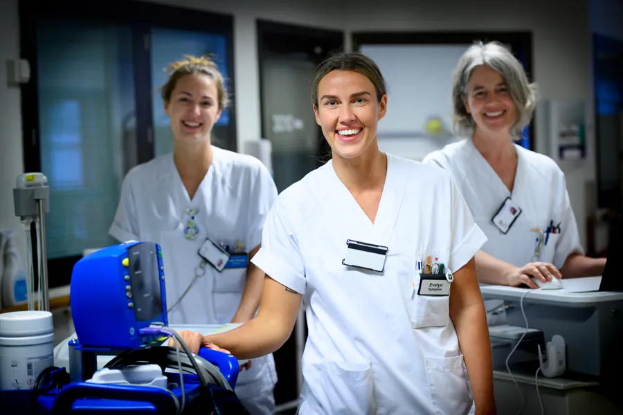 Tre sykepleiere smiler i en gang. Foto.