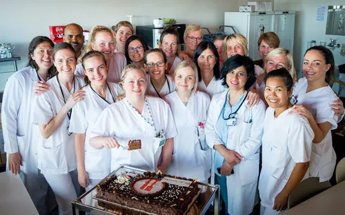 En gruppe mennesker i hvite labfrakker står foran en kake
