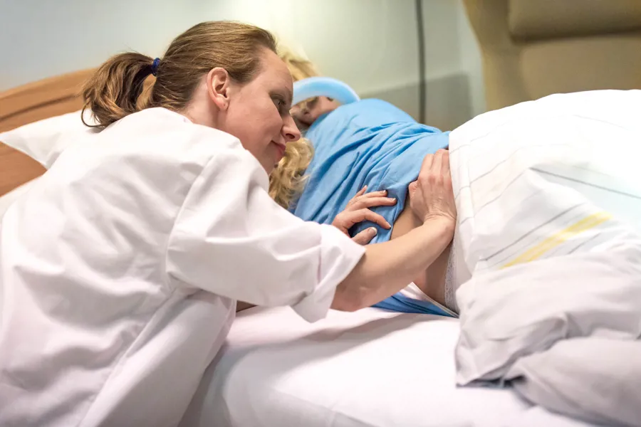 Jordmor holder på ryggen til en kvinnelig pasient i en seng