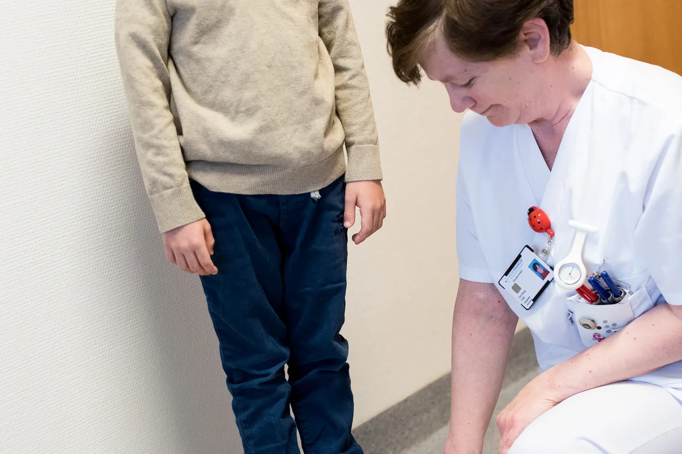 Liten gutt som står på en vekt. Sykepleier i hvite klær ser på vekten. Foto.