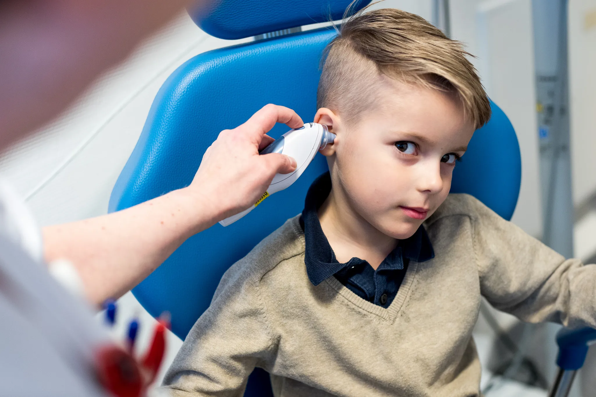 Liten gutt måler temperaturen i øret med et øretermometer. Foto.