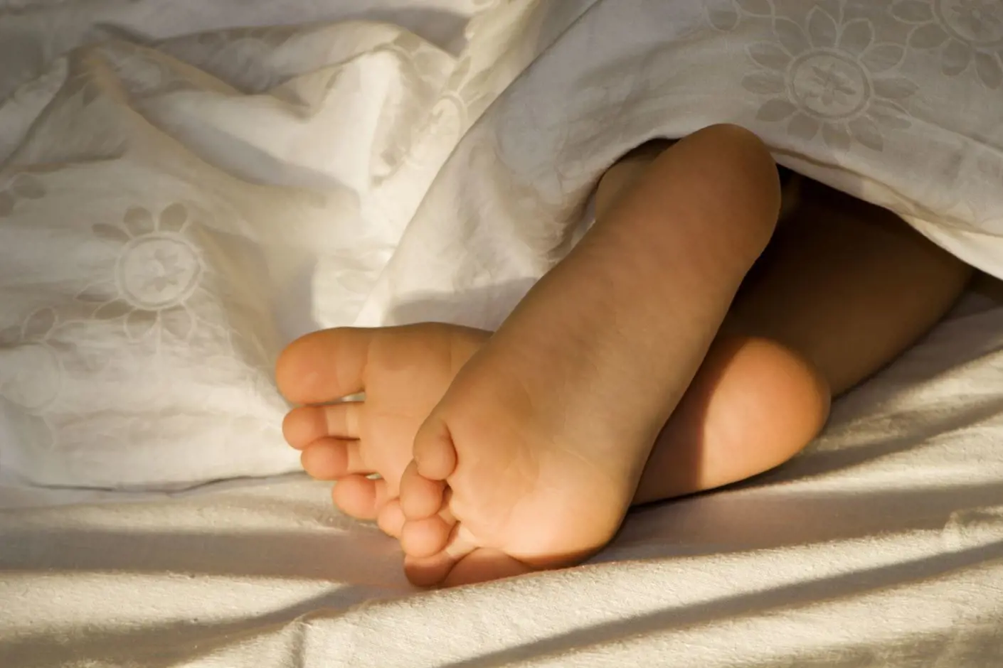 Et barn ligger under dynen i sengen med føttene ute