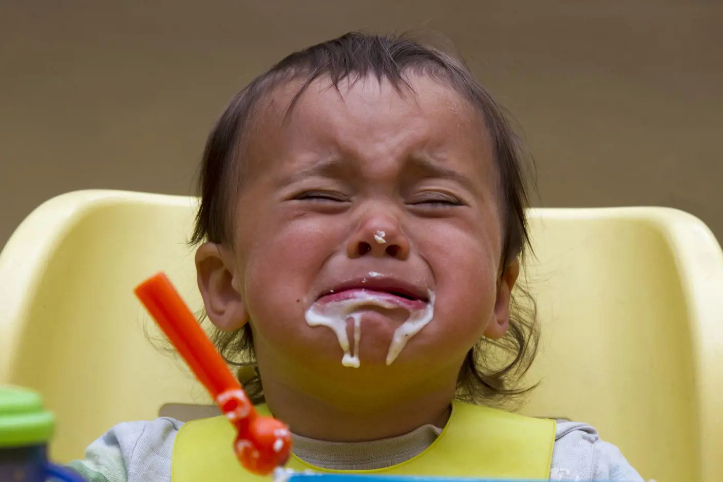 Et lite barn som gråter mens det spiser med masse søl rundt munnen