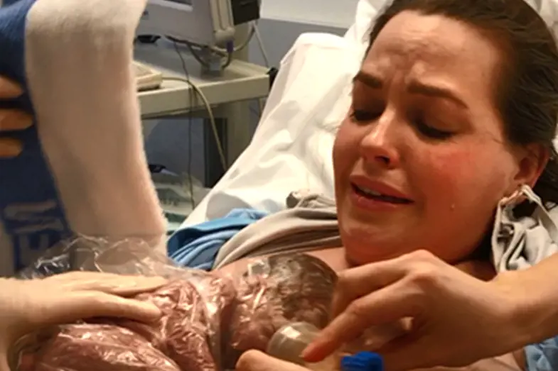 En kvinne har sitt nyfødte premature barn inntril brystet og gråter
