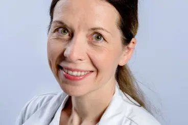 Kvinne i legeuniform smiler til kameraet. Foto.