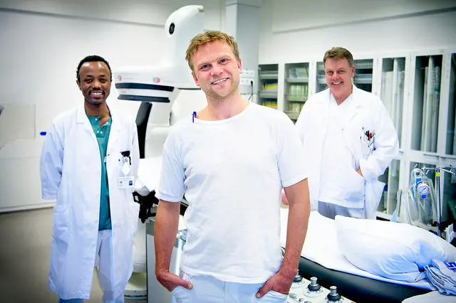 Tre hvitkledde menn står på en rekke og smiler inn i kamera.