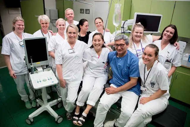 12 sykehusmedarbeidere holder rundt hverandre og smiler.