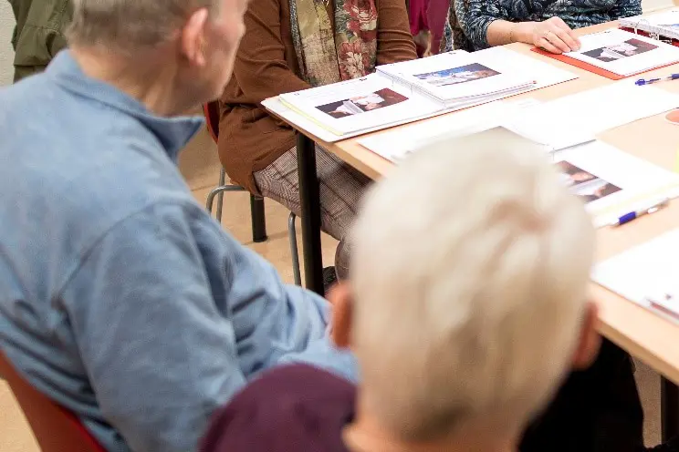 Deltakere i demensskolen som sitter rundt et bort. Bilde.