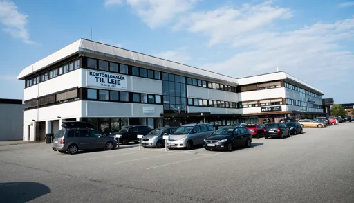 Hvitt, langt hus med parkeringsplass foran.